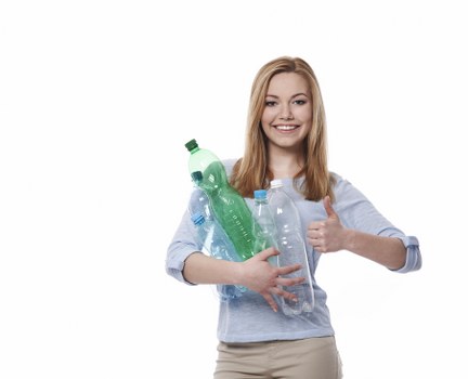 A young woman with long, straight blonde hair and a friendly smile is holding several plastic bottles, including a green, a clear, and a blue one, close to her chest. She is giving a thumbs-up with her right hand. She is wearing a light blue, long-sleeved shirt with sleeves rolled up slightly and beige trousers. The background is plain white, emphasizing her presence and the bottles she is holding. The scene appears well-lit with soft, even lighting. This image relates to waste management and recycling services, reflecting environmentally conscious practices, potentially in the Chislehurst area. It visually conveys the theme of rubbish collection and recycling, aligning with services offered by Commercial Waste Removal Chislehurst for proper disposal and environmentally responsible waste management.
